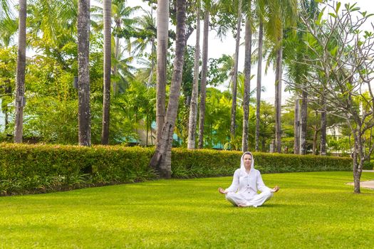 Caucasian woman practicing yoga on a green lawn