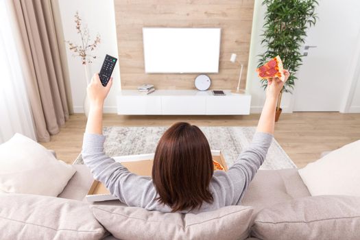 Woman sitiing on couch eating pizza and watching tv