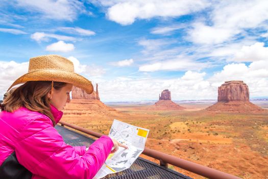 Woman wearing cowboy hat sitting and looking at map in Monument Valley with red rocks overview in Arizona USA