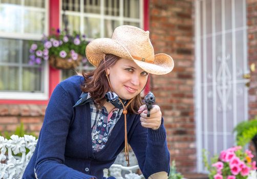 Country style portrait of a beautiful brunette young woman with a gun and cowboy hat