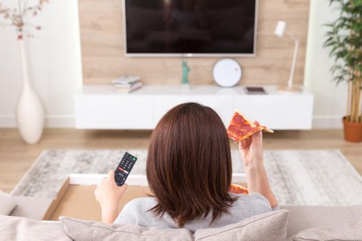 Woman sitiing on couch eating pizza and watching tv