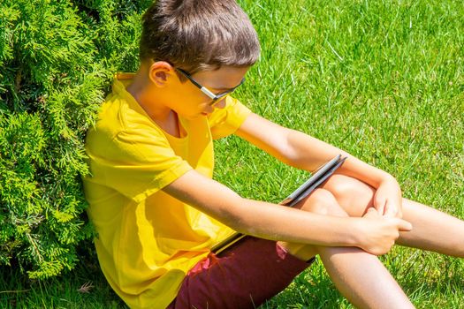 Boy with tablet PC on green grass lawn