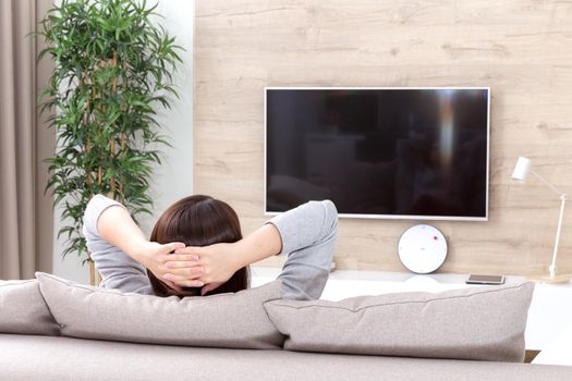 Young woman watching TV in living room with crossed arms. black screen with copy space