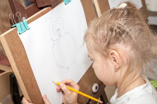 Little girl painting picture on easel in classroom