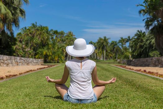 Woman doing yoga exercises in park sitting in lotus posture