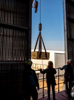 The crane carrying a wooden box of the radioactivity holder into the window on the factory floor