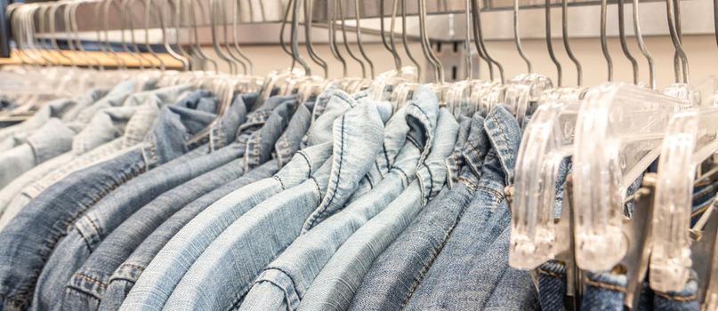 Male mens denim jeans shirts sorted on clothes hangers on a shop wardrobe closet