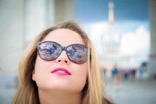 Cute girl in sunglasses. The clouds are reflected in the glasses. Happy girl face close up.