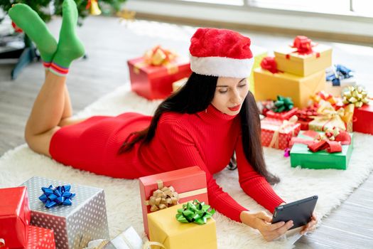 Top down view of Caucasian woman with Christmas costume lie on carpet in room near the present or gift box and she also use tablet.