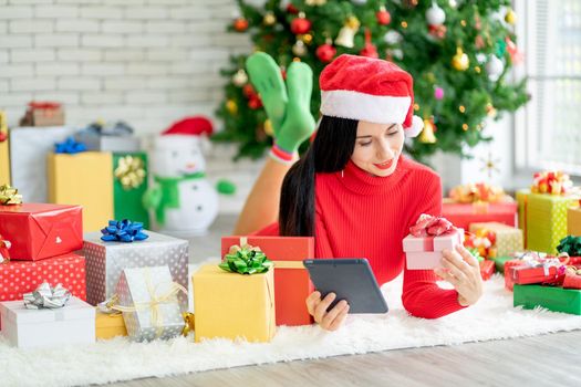 Woman with Christmas costume lie on floor of living room of her house and hold gift box and tablet look like online shopping.