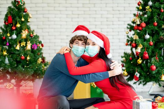 Couple man and woman with hygiene mask hug together and look at camera for celebrating of Christmas festival during pandemic of Covid-19.