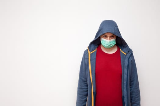 Man with green protective mask on white background. A man with a red sweater and a blue jacket, with a hood.