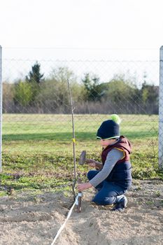 A boy hammers a stake with a hammer in the garden to mark the garden