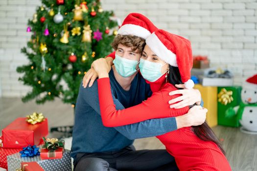 Couple man and woman with hygiene mask hug together and look to the left for celebrating of Christmas festival during pandemic of Covid-19.