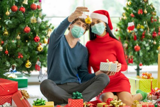 Main focus of gold Christmas ball decorating of Christmas tree that hold by man with hygiene mask and sit near his couple woman during celebration of the festival with new normal lifestyle from covid.