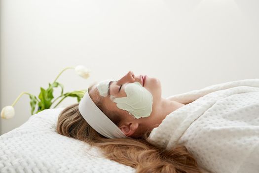 Cosmetologist applying rejuvenating clay facial mask on a female face in beauty salon. Facial treatment concept