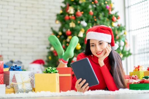 Beautiful woman with rest one or s hands hold tablet and stay in room with Christmas tree look like she happy with online shopping at home during Christmas festival.