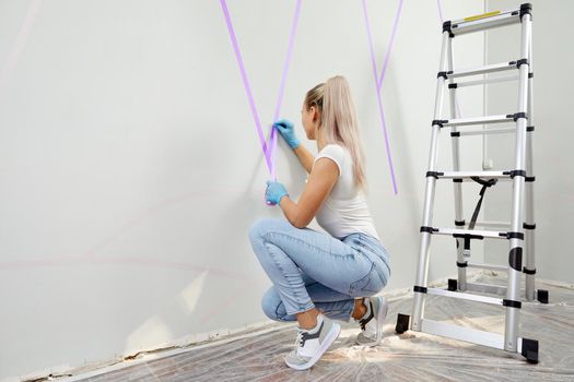 Young woman preparing wall for painting standing on ladder. Diy project with copy space