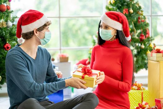 Caucasian man with hygiene mask give the present or gift to his couple woman for Christmas celebration during pandemic of Covid-19 to stay at home of new normal lifestyle.