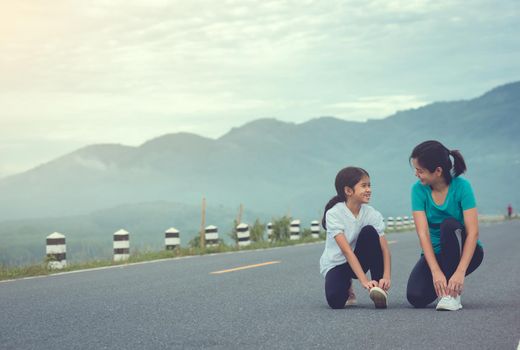 Mom and child are kneeling and tying shoelace. We getting ready for jogging outdoors the time during sunrise on dam road exercise.