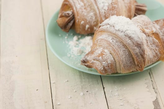 Two fresh croissants in plate on white wooden table. Breakfast