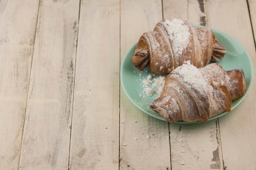 Two fresh croissants in plate on white wooden table. Breakfast