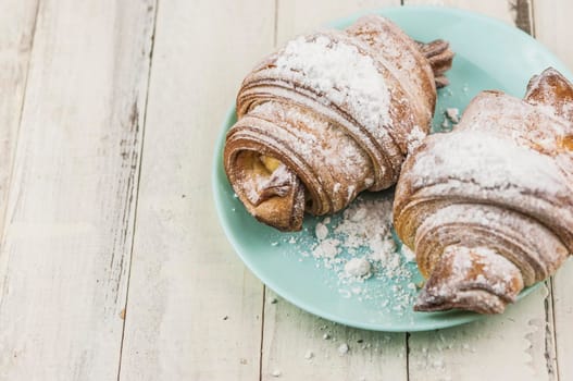 Two fresh croissants in plate on white wooden table. Breakfast