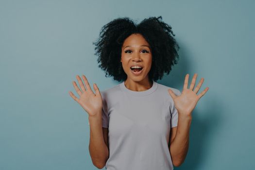 Studio shot of excited dark skinned woman showing palms at camera and demonstrating optimism, feeling happy and overjoyed while standing isolated over blue background. Positivity concept