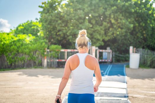 Fitness woman listening to music in sportswear with wireless in-ear headphones on summer ocean beach