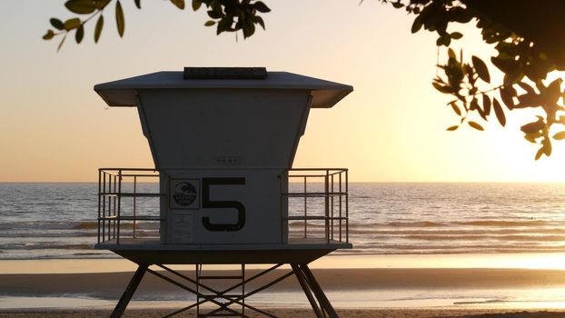 Lifeguard watch tower, sunny sunset beach, Oceanside USA. Rescue station, waterfront watchtower hut and tree leaves, pacific ocean coast atmosphere. California summertime aesthetic, Los Angeles vibes.