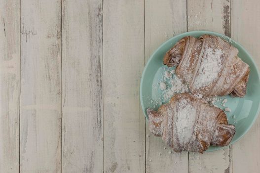 Two fresh croissants in plate on white wooden table, top view