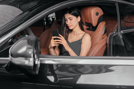 Young attractive asian woman using phone while sitting in a new luxury car front sea