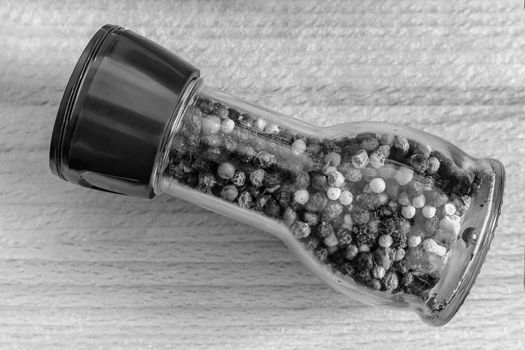 A set of spices: black, white, red pepper peas in a glass bottle on a wooden table. Front view, copy space