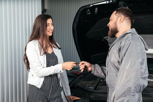 Car mechanic giving client keys to her repaired car in auto repair service