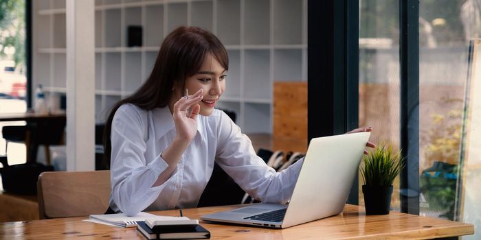 Cheerful young asian woman using laptop computer at home. Student female in living room. online learning, studying , online shopping, freelance, asean concept.