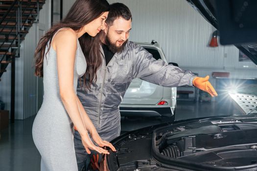 Car mechanic and customer stand next to the serviced car. The car had an annual checkup and stands in the garage with the hood open