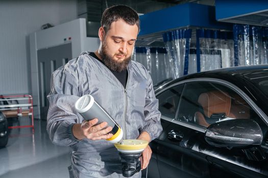 Worker polishing vehicle body with special grinder and wax from scratches at the car service station