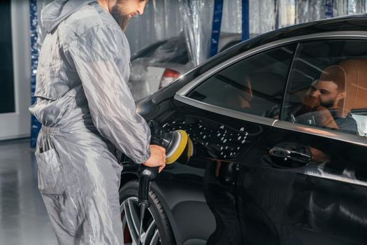 Worker polishing vehicle body with special grinder and wax from scratches at the car service station