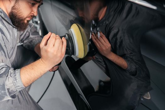 Worker polishing vehicle body with special grinder and wax from scratches at the car service station