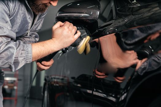 Worker polishing vehicle body with special grinder and wax from scratches at the car service station