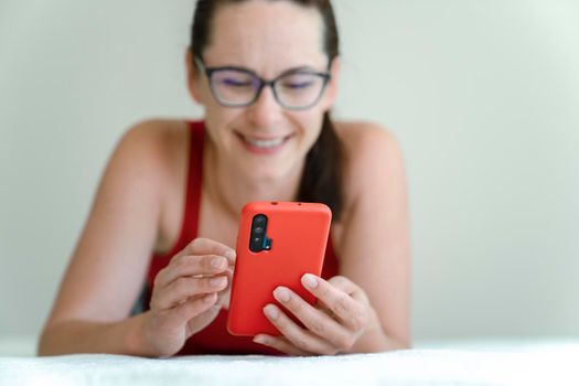 Young woman talk via video chat with positive emotions on her face while lying on bed.