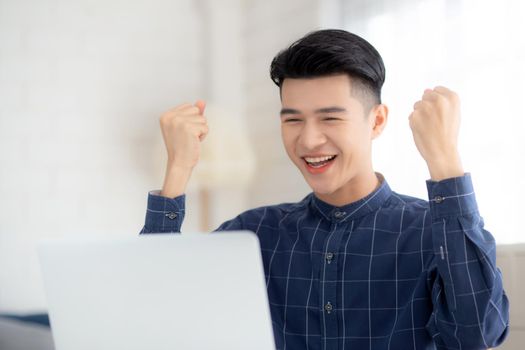 Happy young businessman work on laptop computer finish with excited and success on desk at home, business man using notebook with achievement and surprised, freelance or employee, satisfied and glad.