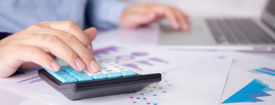 Hands of businessman calculate tax with calculator while laptop computer on desk, man planning finance and investment with graph and chart, statistic and examining account, business concept.