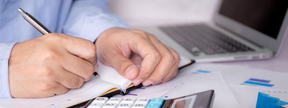 Hands of businessman calculate tax with calculator while laptop computer on desk, man planning finance and investment with graph and chart, statistic and examining account, business concept.