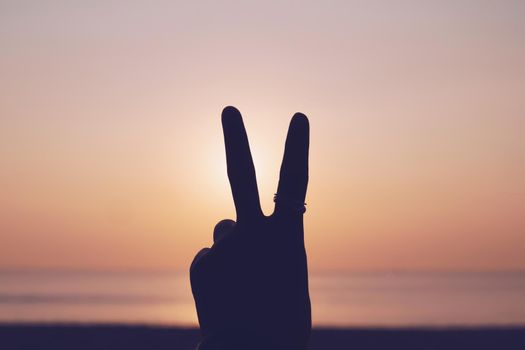 Peace out or fighting metaphor two fingers hand sign in front of a sunset. Happy people enjoying nature. 