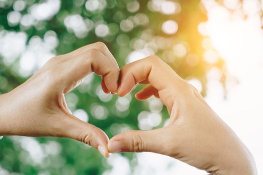 Woman hand do heart shape on green bokeh nature background.