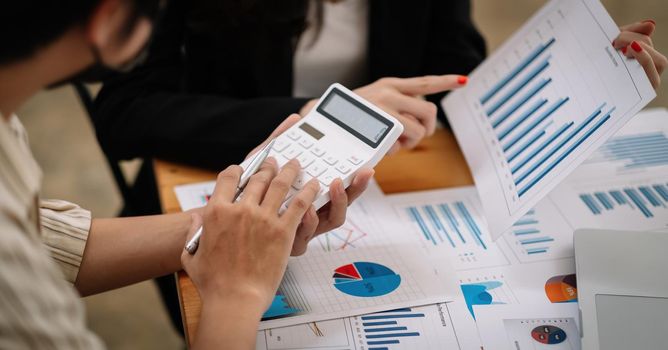 Business team using a calculator and laptop computer to calculate the numbers on his desk in a office