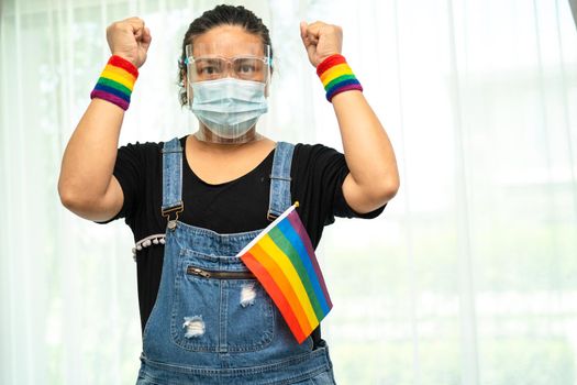 Asian lady wearing blue jean jacket or denim shirt and holding rainbow color flag, symbol of LGBT pride month celebrate annual in June social of gay, lesbian, bisexual, transgender, human rights.