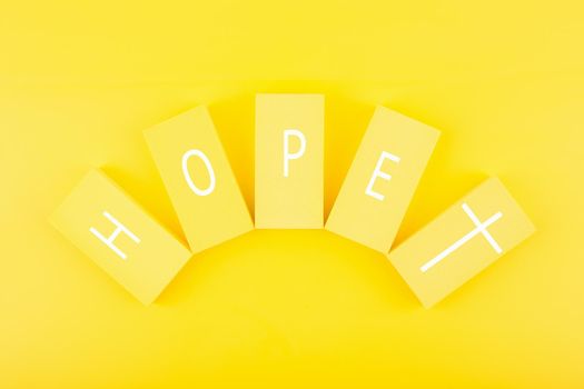 Modern religious minimal concept of hope with christian cross on bright yellow background. Biblical creative composition with single word hope and cross