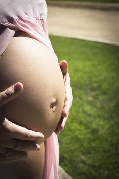 Seven month pregnant woman in pink transparent dress holding belly. Natural background